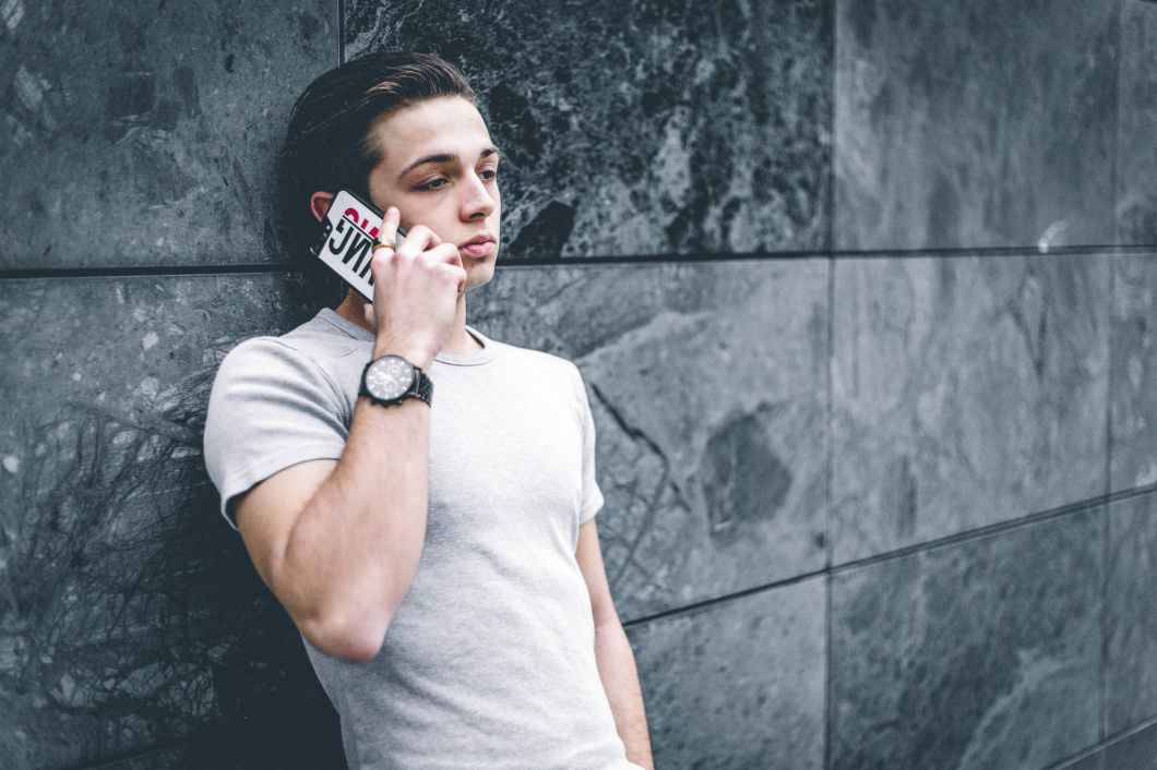 man wearing gray crew neck t shirt leaning on gray wall