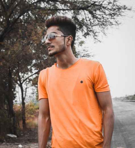 man standing while wearing orange crew neck shirt near tree