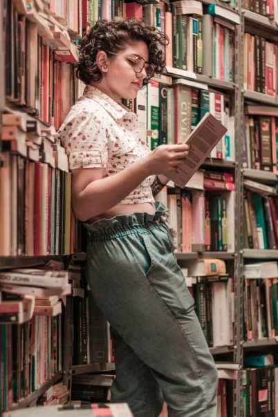 woman holding book leaning on books on shelves